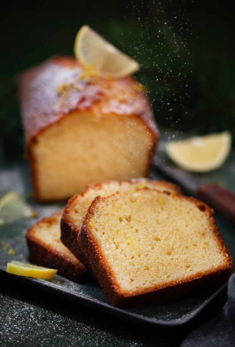 homemade lemon pound cake loaf sliced with powdered sugar and fresh lemon